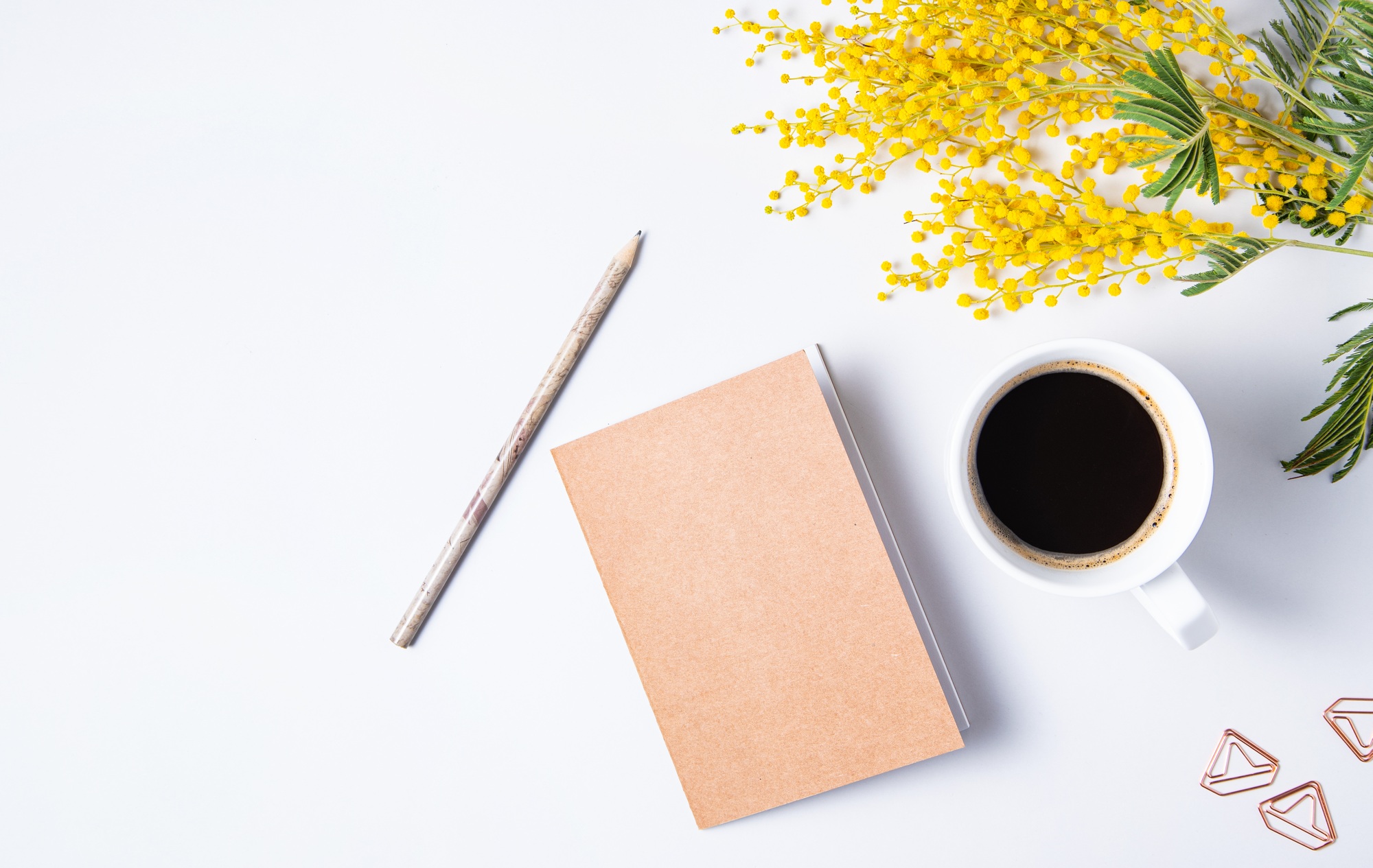 Flat lay with yellow mimosa flower, cup of coffee, craft notebook and pencil on a marble table